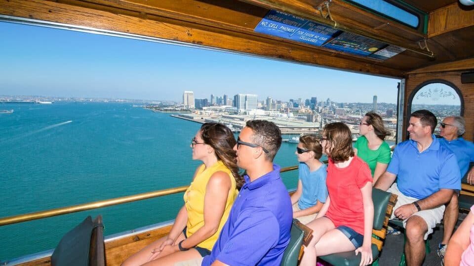 Pessoas sentadas dentro de um ônibus panorâmico, observando o mar de San Diego e toda a cidade.