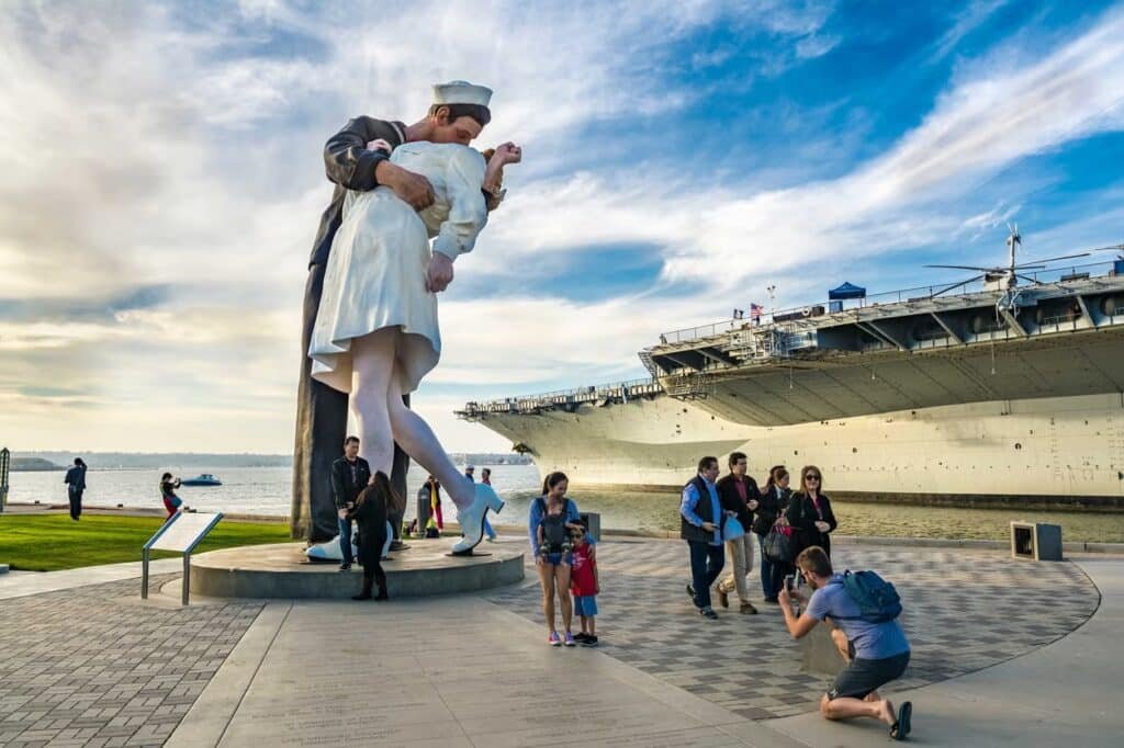 Foto da estátua "Unconditional Surrender", em que um soldado beija uma enfermeira. Ela é bem grande e está ao lado do navio.