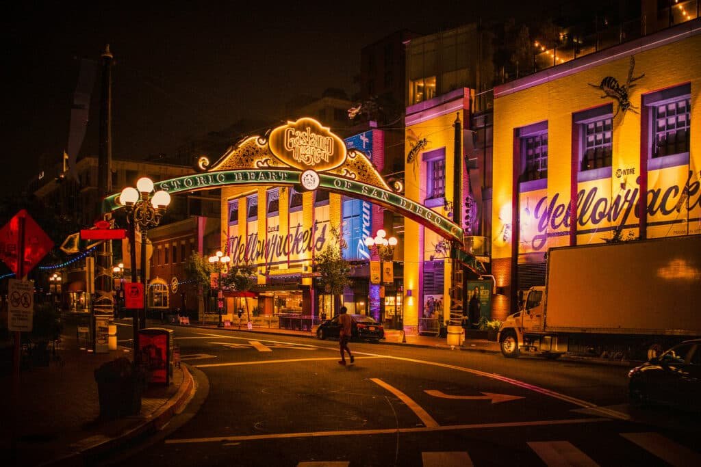 Uma placa iluminada escrito “Gaslamp Quarter” indica a entrada do bairro. Várias construções também iluminadas estão ao redor. É possível ver também carros e caminhões estacionados. Esta foto ilustra o post de o que fazer em San Diego.