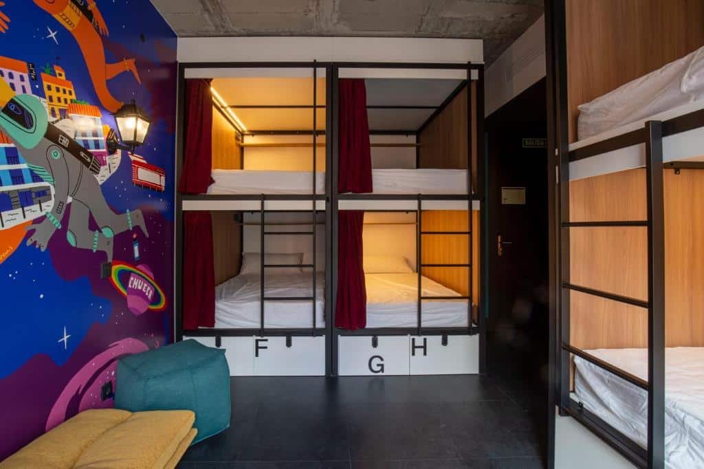 Beliches numeradas no hostel The Central House Madrid Lavapiés. A parede esquerda tem uma pintura colorida e bancos estofados logo abaixo.