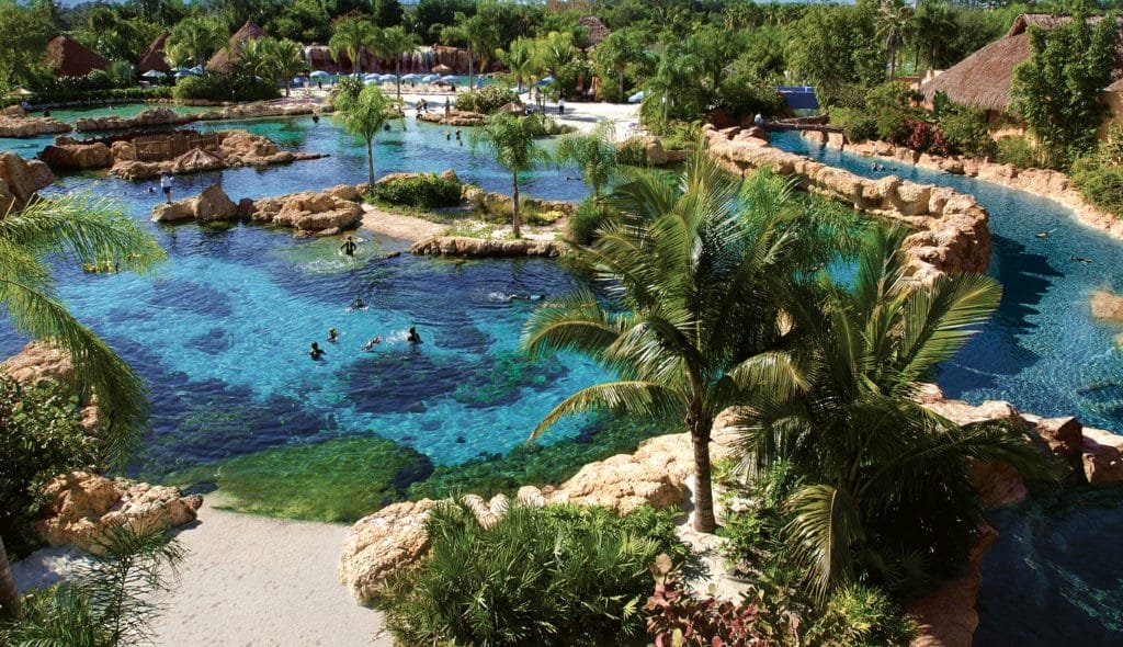 Foto panorâmica do parque Discovery Cove, com seus lagos e vegetação, além de pessoas nadando