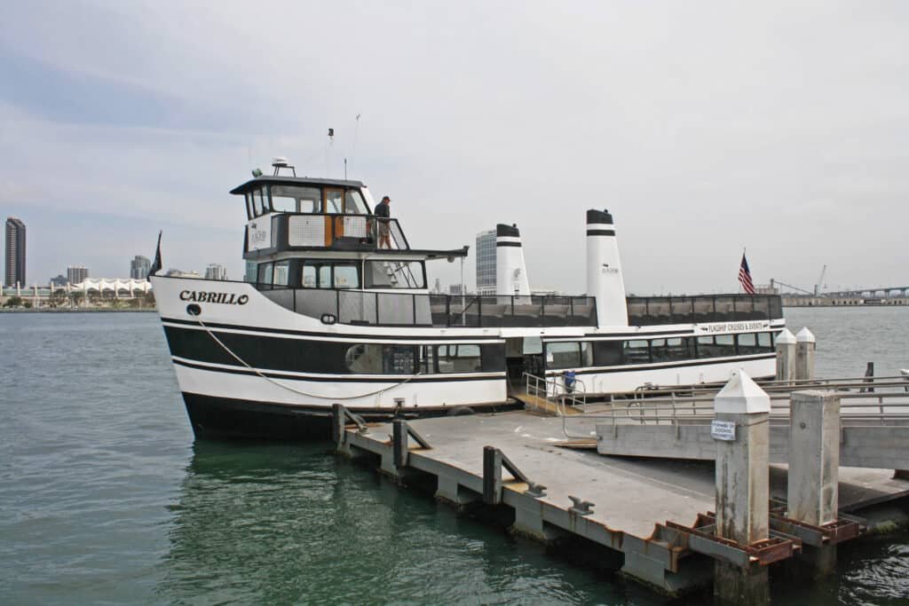 A foto mostra um ferry que faz o trajeto entre San Diego e a Ilha de Coronado atracado no píer. O píer e o ferry estão em primeiro plano. Ao fundo está a cidade.