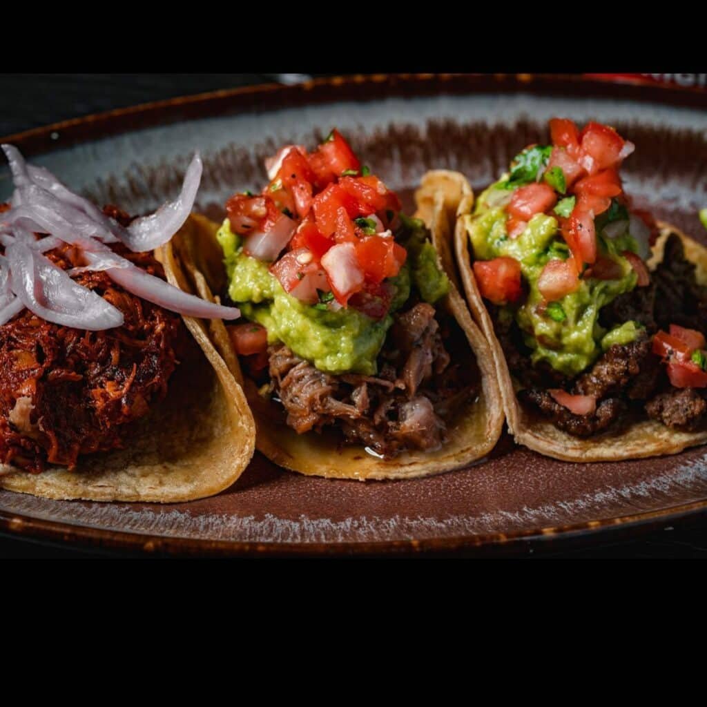 Um prato com três tacos de carne com vegetais do La Puerta.